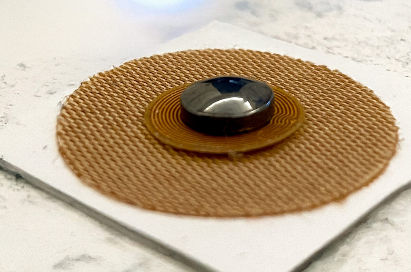 Биотег с NFC-чипом для гармонизации зависимости Круглый биотег из тканевой основы с NFC-антенной и металлическим магнитом в центре на белой подложке
